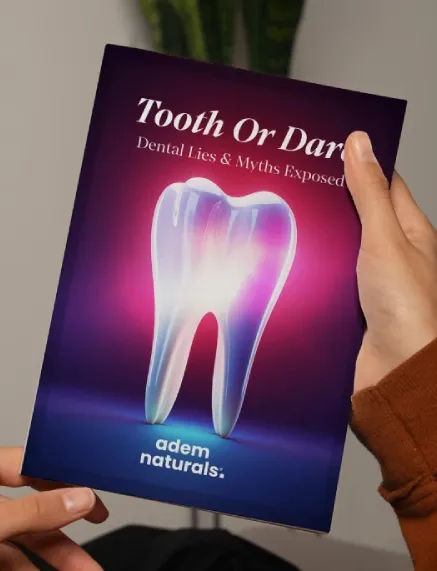 Person holding a book titled ‘Tooth or Dare: Dental Lies & Myths Exposed’ by Adem Naturals, featuring a glowing translucent tooth on a dark purple and pink background.